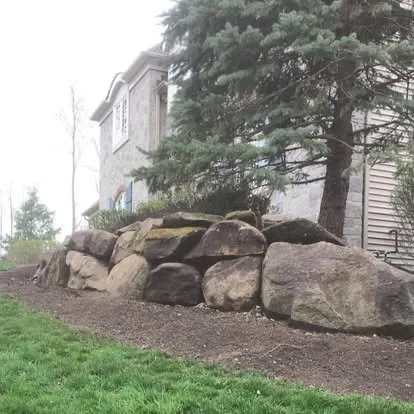 Natural boulder retaining wall along stone home